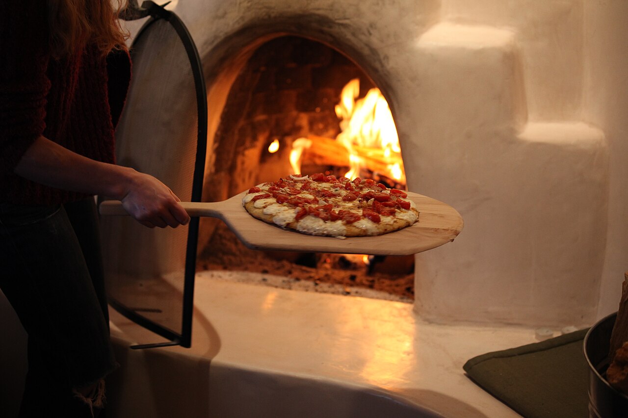 Una pizza appena sfornata sulla pala, davanti al forno
